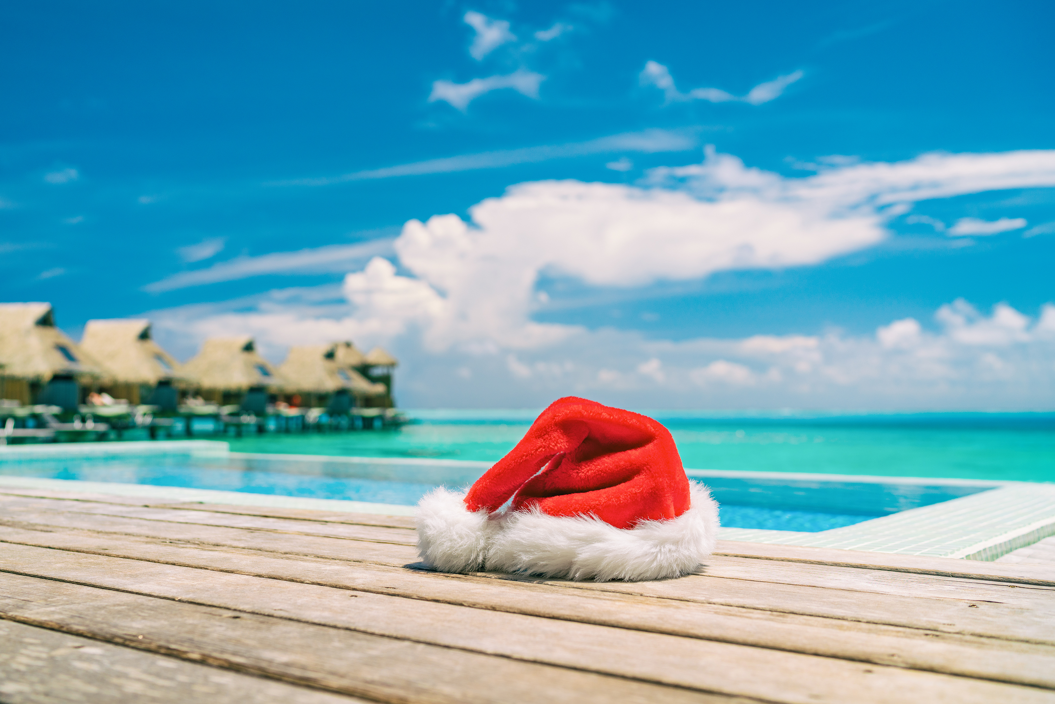 Christmas Santa Claus hat by the swimming pool at luxury vacation resort for high end summer destination sun vacation getaway during winter holiday. Overwater bungalows villas.